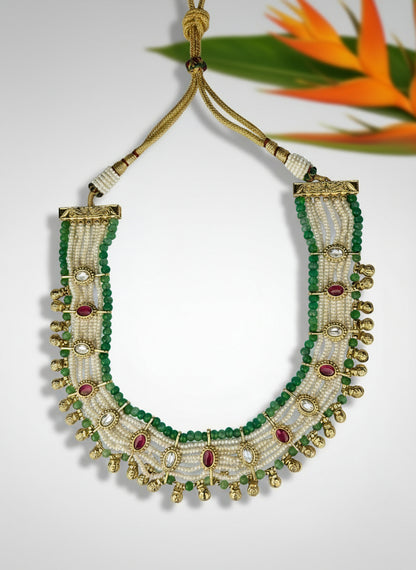 Ornate necklace with green, gold, and red beads on a light gray background